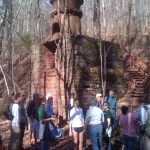 Group of people standing in a forested area, in front of an old mining installation.